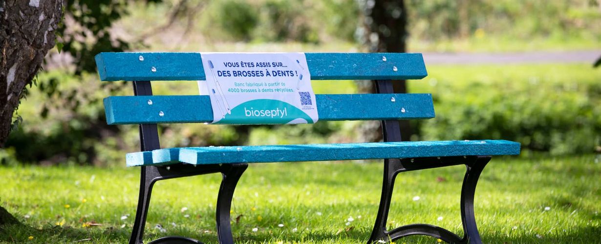 Banc bleu avec la mention "Vous êtes assis sur ... des brosses à dents ! Banc fabriqué à partir de 4000 brosses à dents recyclées. BIOSEPTYL"