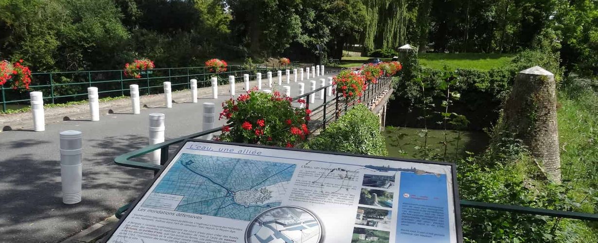 Photo des berges des wateringues, avec un panneau explicatif sur l'eau